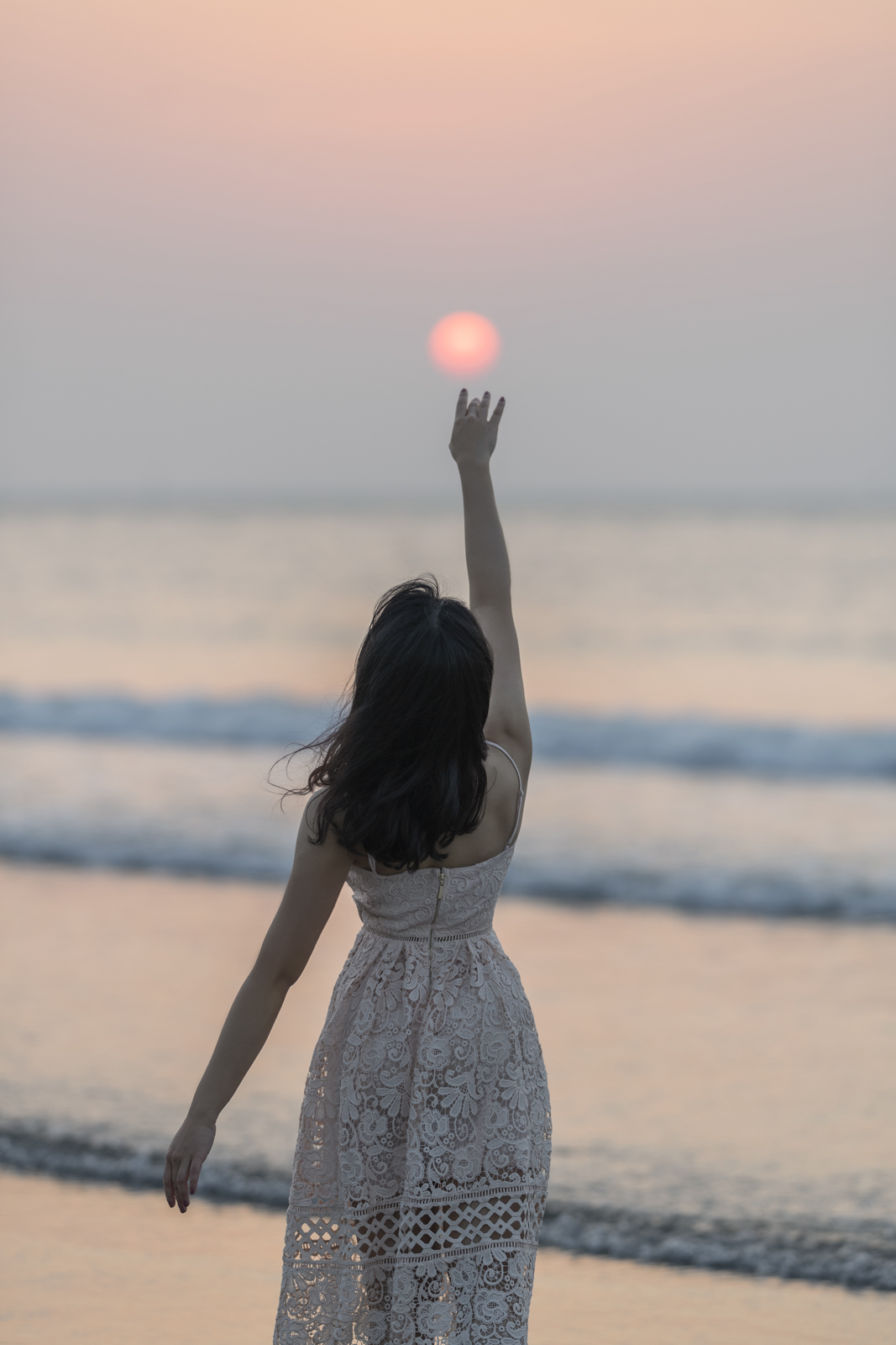 女孩在海邊伸手觸碰夕陽的剪影畫面
