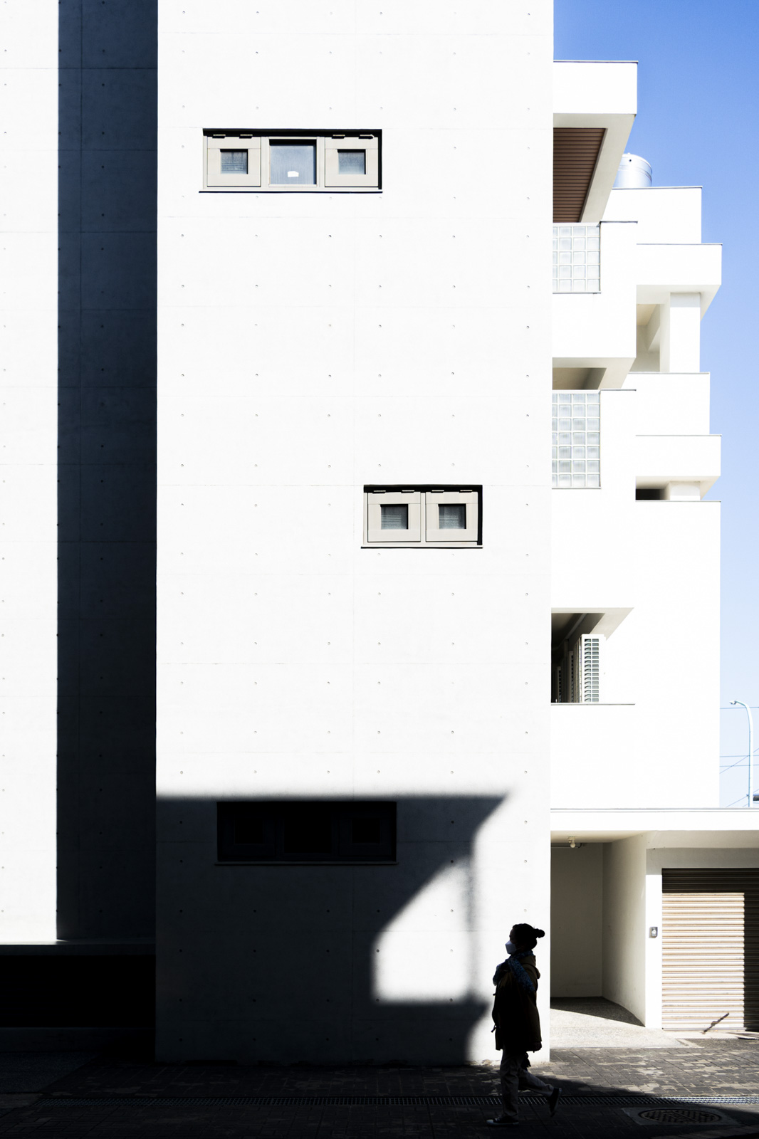 街頭女子走過建築陰影,日光與建物投射出強烈幾何感