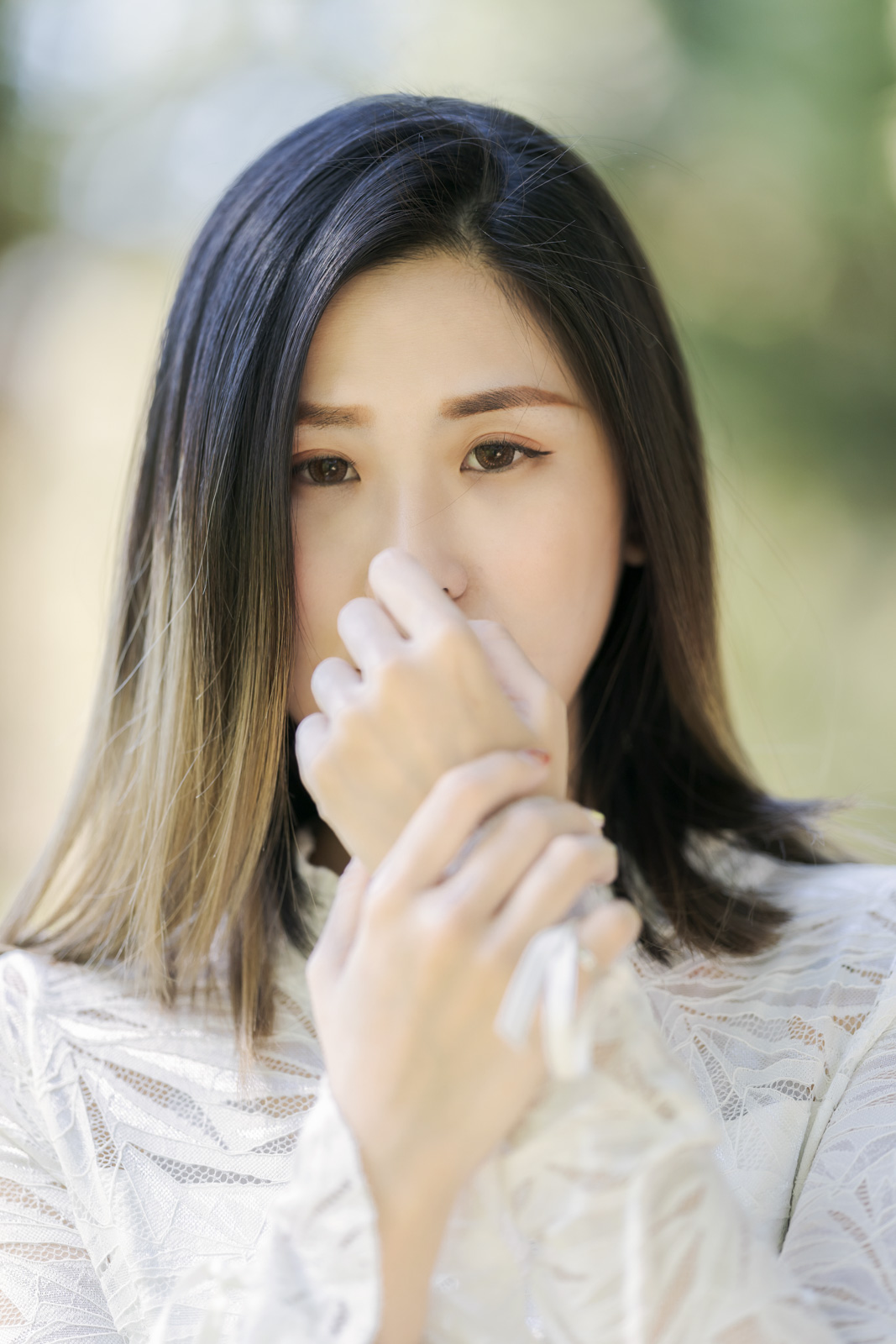 女性眼神凝視鏡頭,雙手輕觸面頰,背景柔焦呈現森林光斑