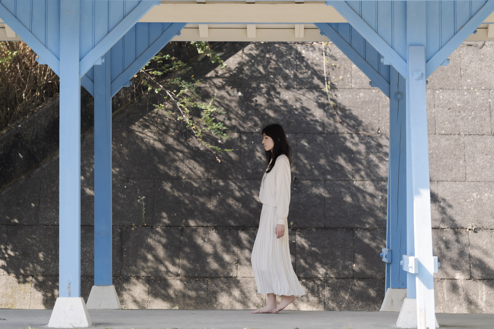 女子走過藍色木構建築下的陰影空間