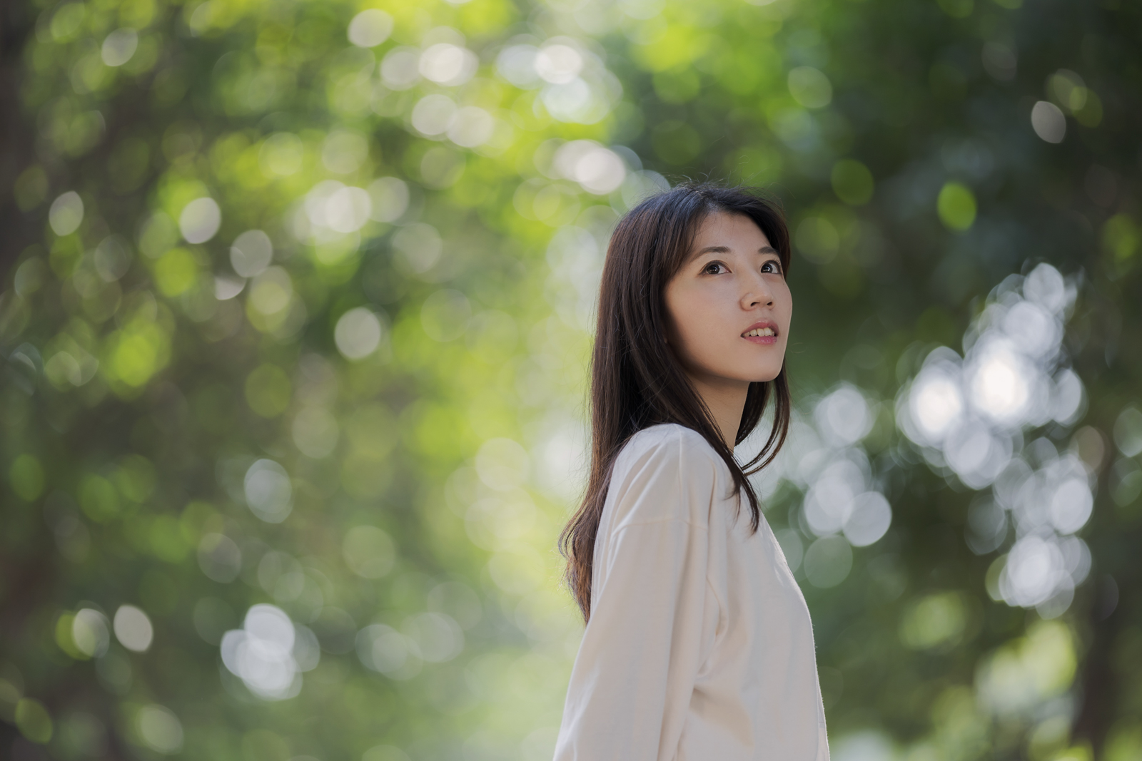 年輕女性望向遠方,背景為柔化綠色光斑
