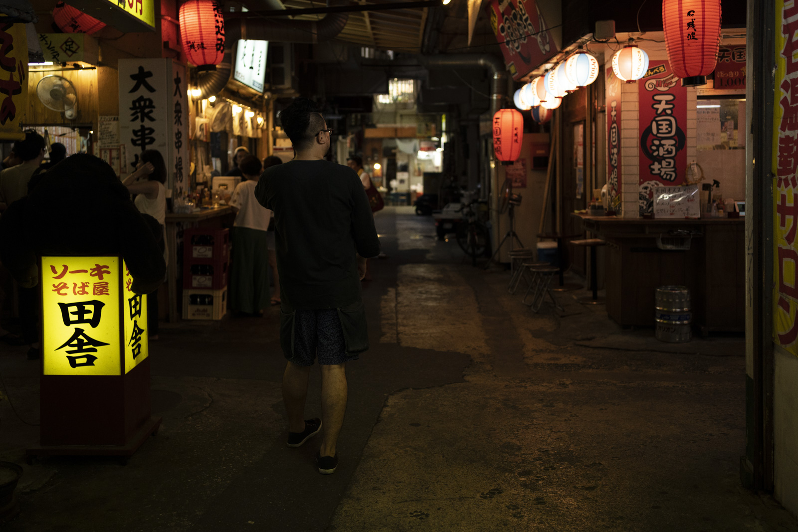沖繩國際通旁的巷弄，午後行人穿梭在居酒屋燈光下的街道場景