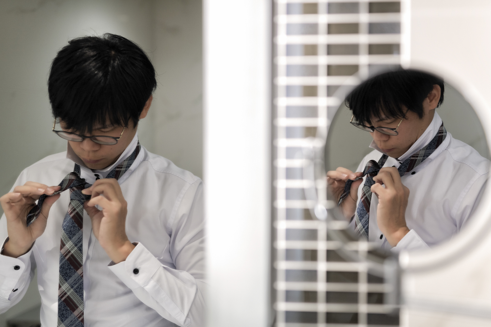新郎專注打領帶的畫面，鏡面呈現雙重構圖