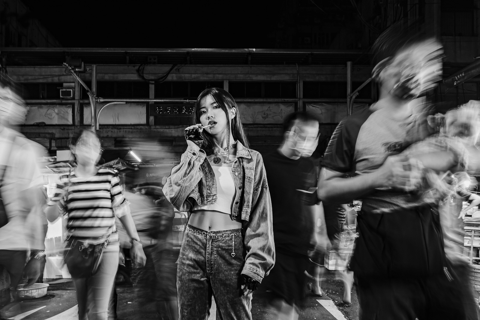 夜市中女孩凝視鏡頭，周圍人群動態模糊黑白對比