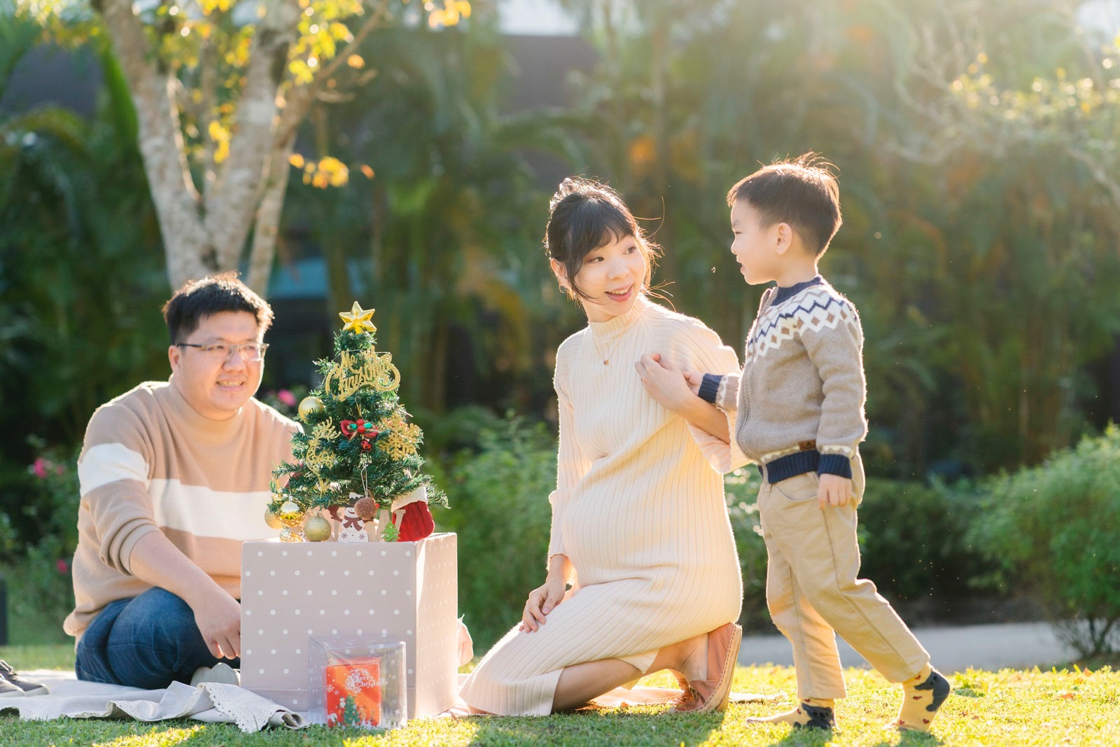 冬日午後陽光下，一家三口在草地上互動，媽媽與孩子對視微笑，爸爸坐在後方陪伴