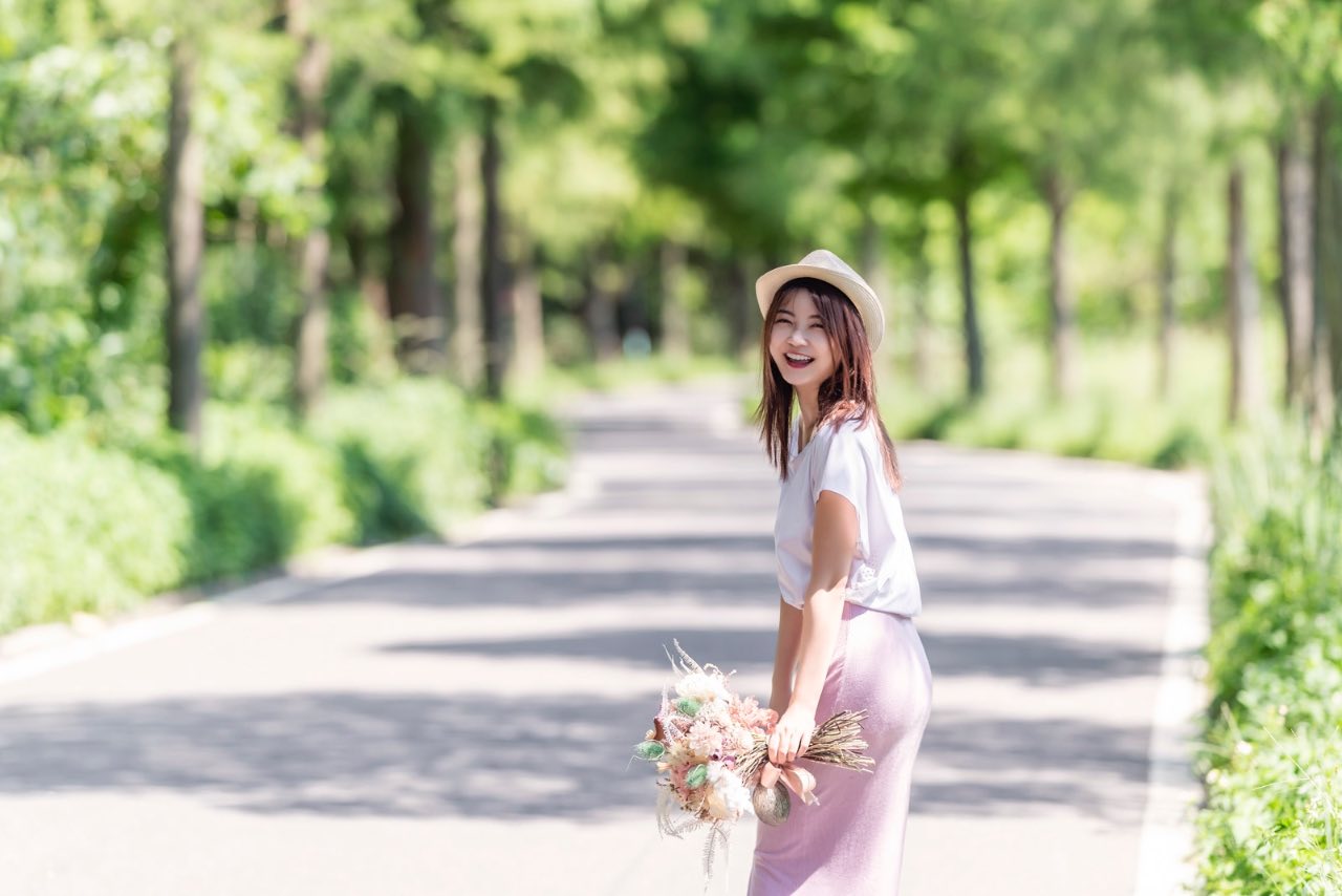 女子在林蔭大道上回眸微笑手拿花束