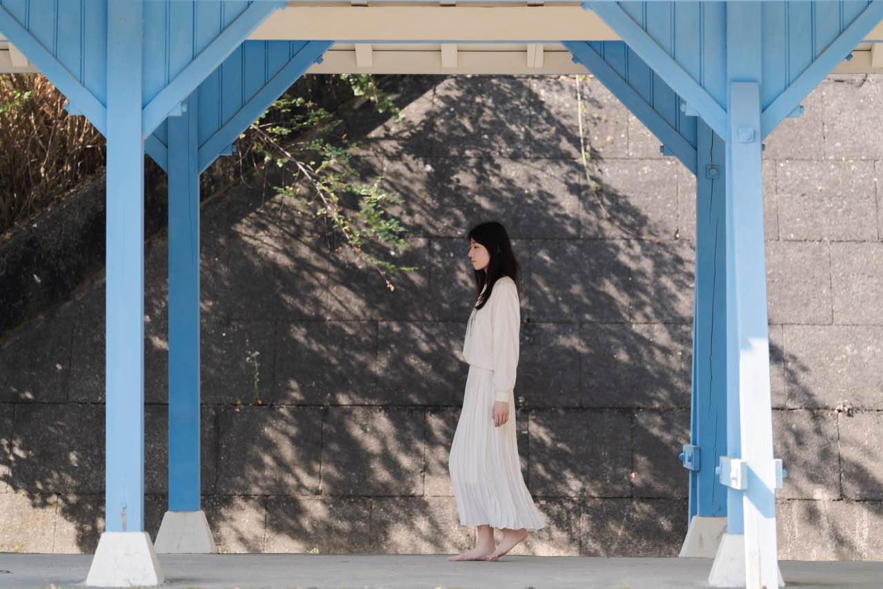 女子走過藍色木構建築下的陰影空