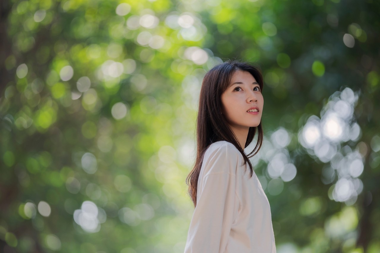 年輕女性望向遠方,背景為柔化綠色光斑