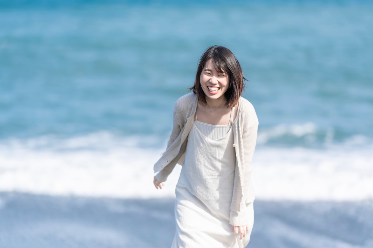 女子迎著鏡頭笑著跑來,背景為海浪與藍色海面。