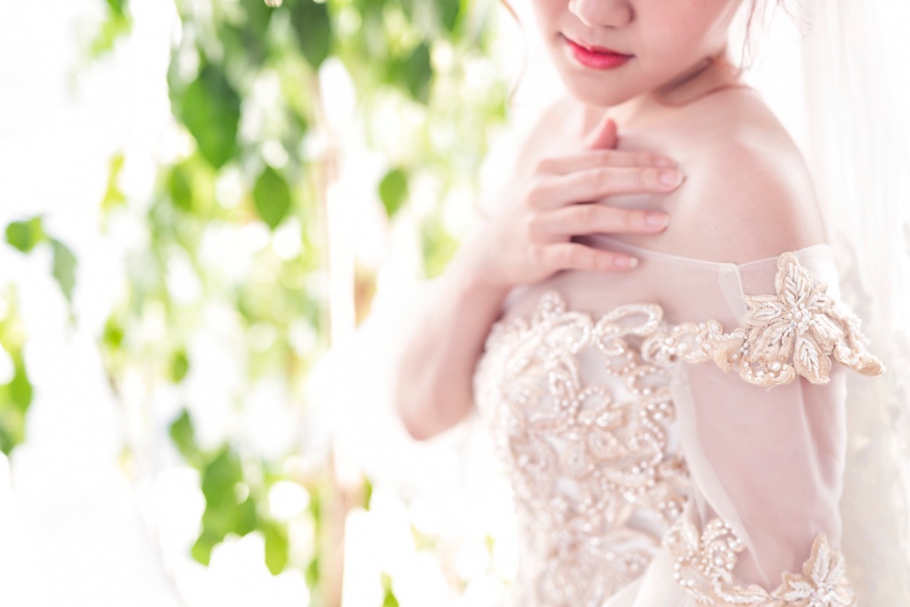 鏡頭聚焦在金色蕾絲婚紗細節，新娘輕扶著自己肩膀