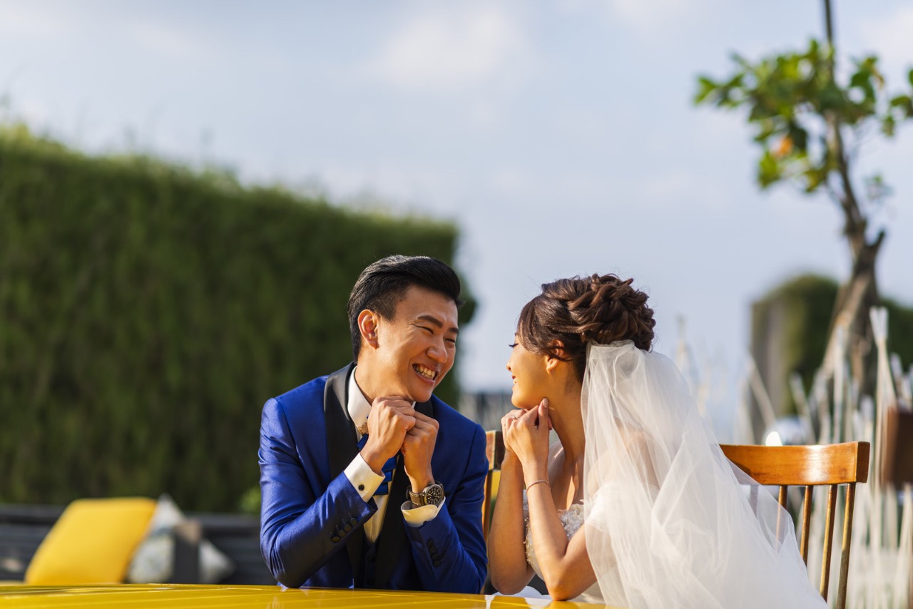 戶外類婚紗中,新人坐在桌旁自然互動並相視而笑