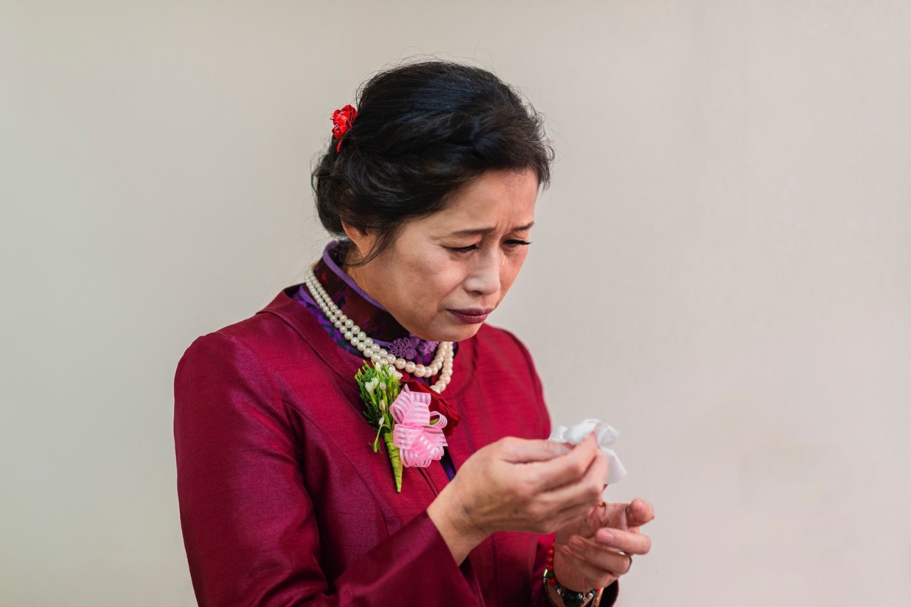 中式婚禮中穿著旗袍的母親低頭拭淚，神情哀傷