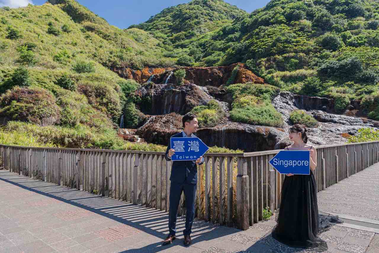 新人手持台灣與新加坡標語牌,在山景瀑布前相對而立