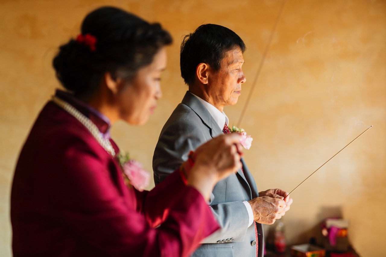 父母在佛前祭拜祖先，手持香火莊重祈願