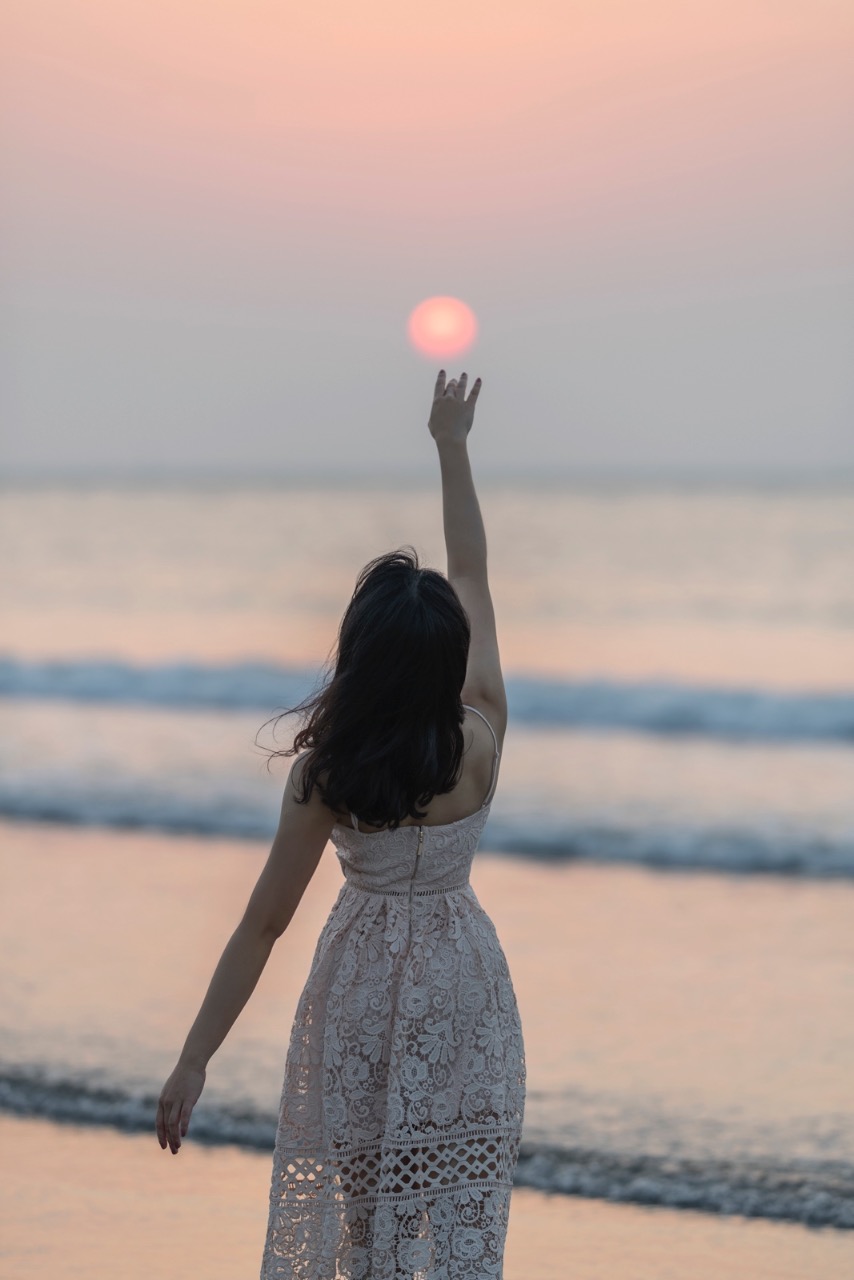 女孩在海邊伸手觸碰夕陽的剪影畫面