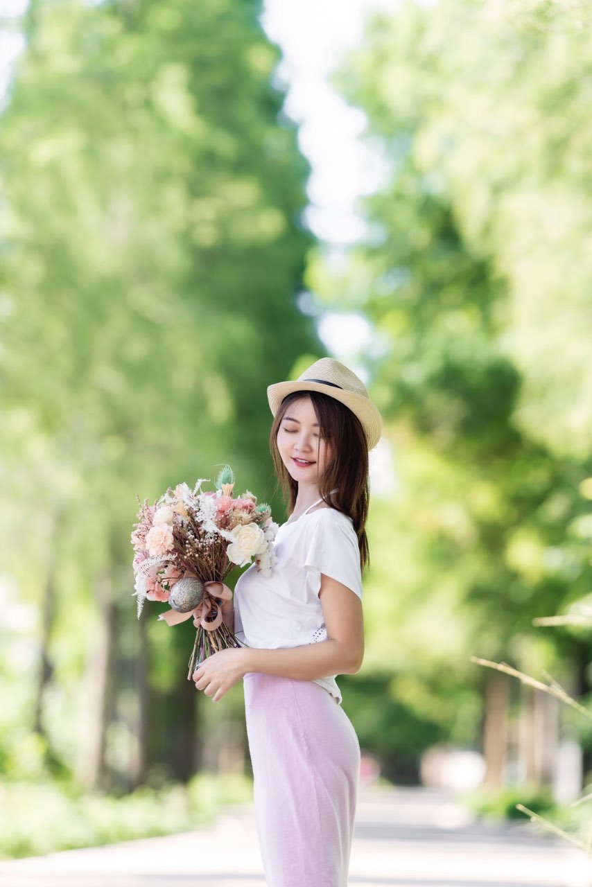 女子側身閉眼手持花束站在鄉間路上