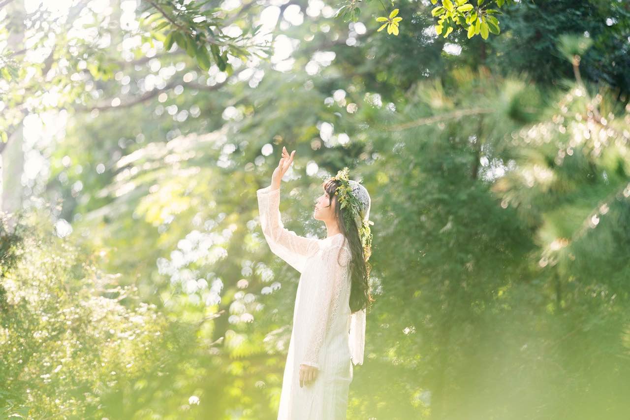 穿著白色洋裝的女子在森林中陽光下舉手感受自然