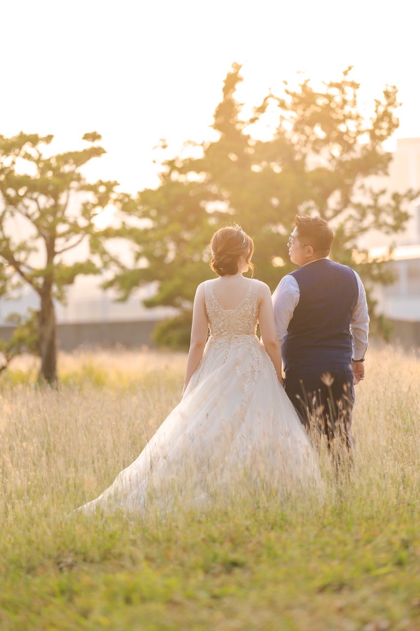 新娘與新郎並肩走在草地上,夕陽照亮婚紗裙擺
