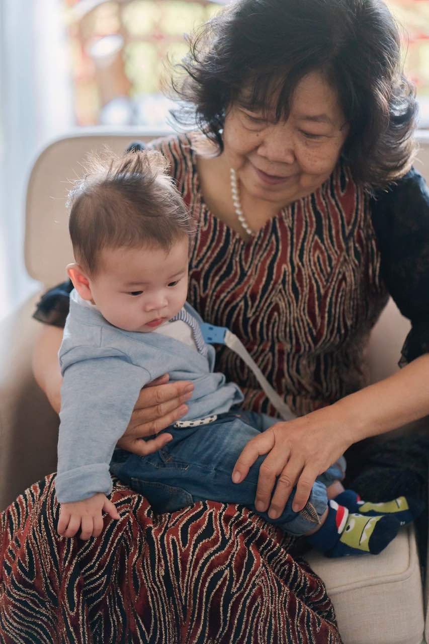 新郎的母親坐在沙發上溫柔抱著小男嬰,低頭微笑