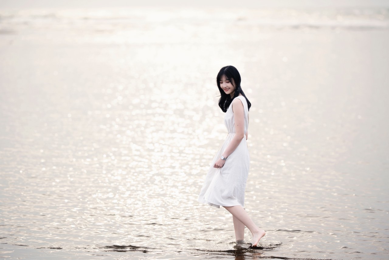 女生一人站在海水中,裙擺搖曳,夕陽映照著水面