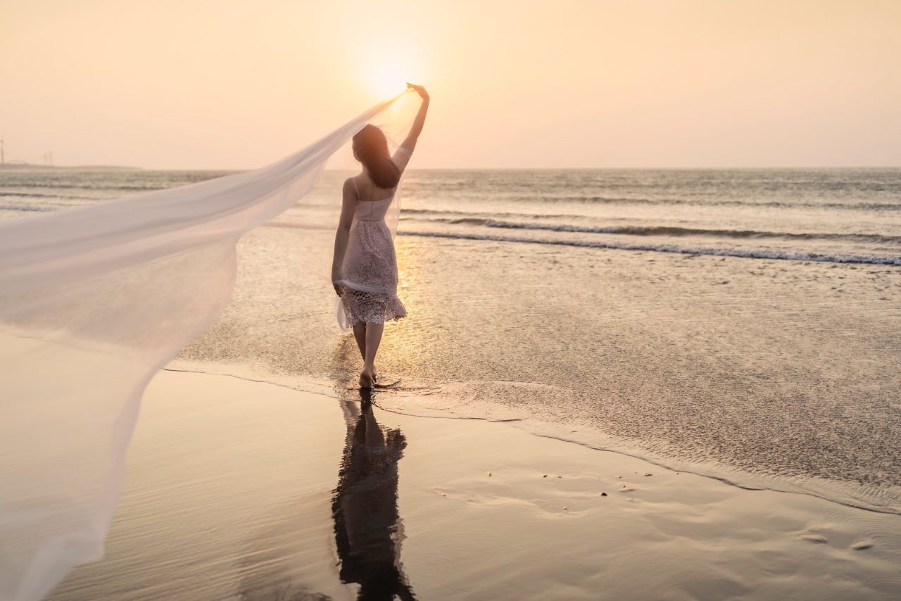 女孩牽著白紗步入海灘夕陽畫面