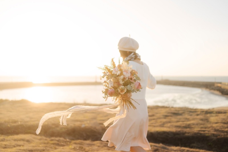 新娘手捧捧花走向夕陽的海岸