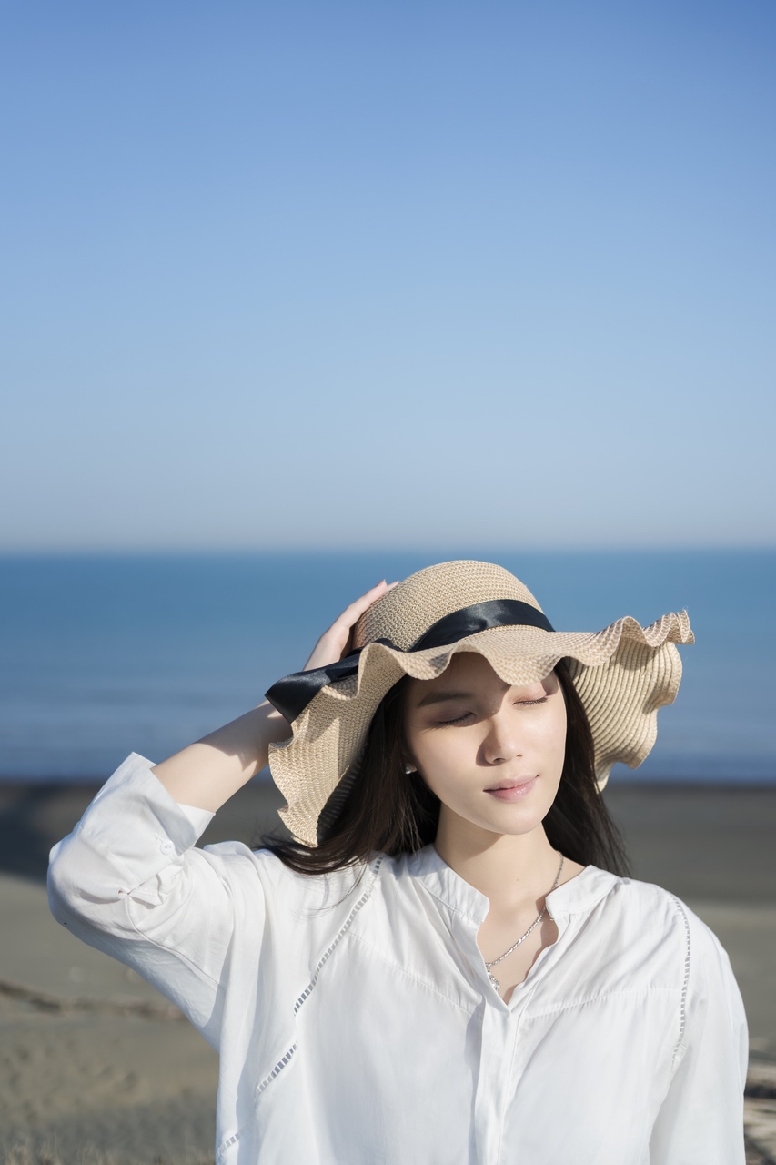 海邊正午的陽光下,女孩戴著草帽閉上眼睛,靜靜感受微風與光線的片刻