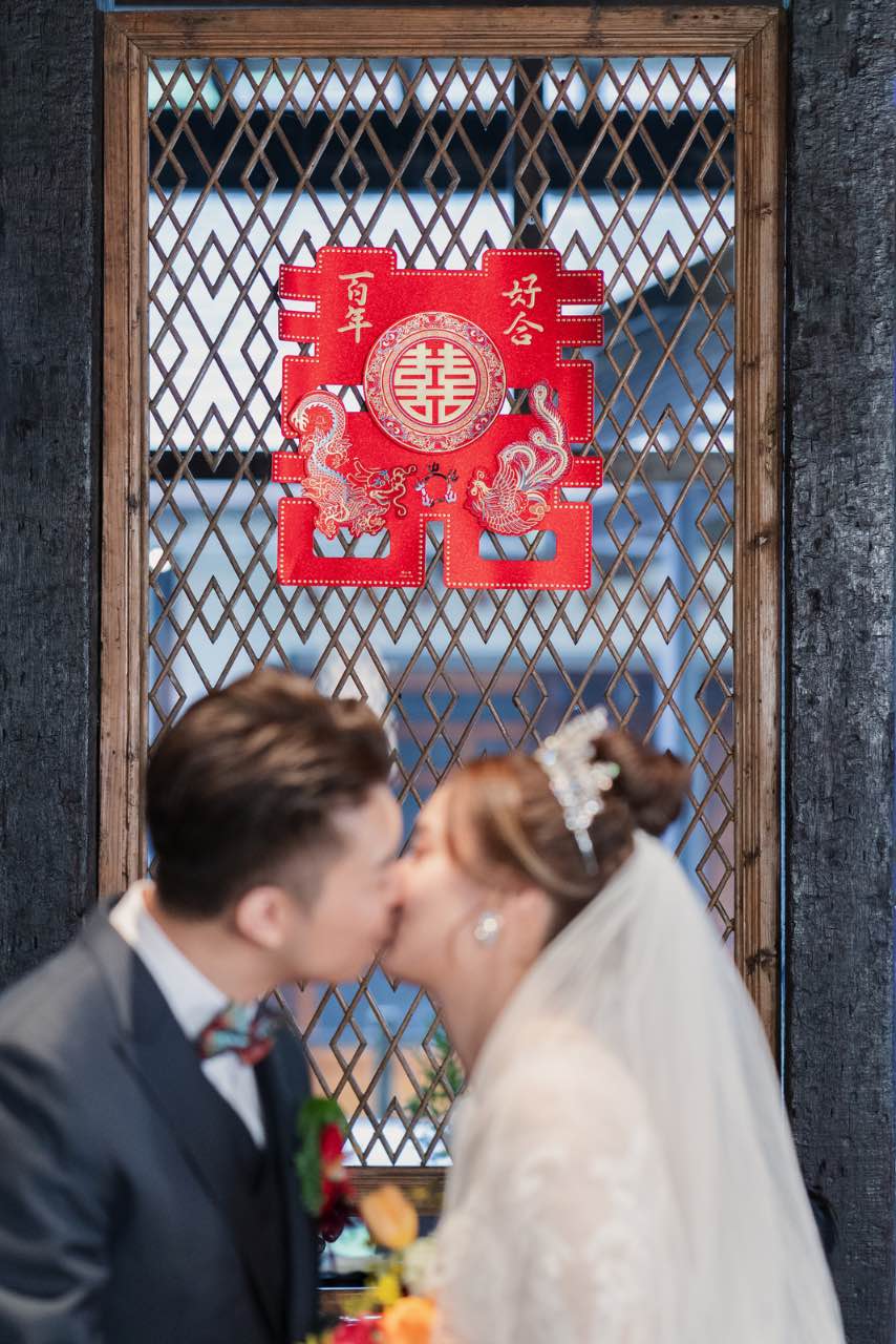 新人在紅色囍字下親吻，象徵新婚的甜蜜時刻