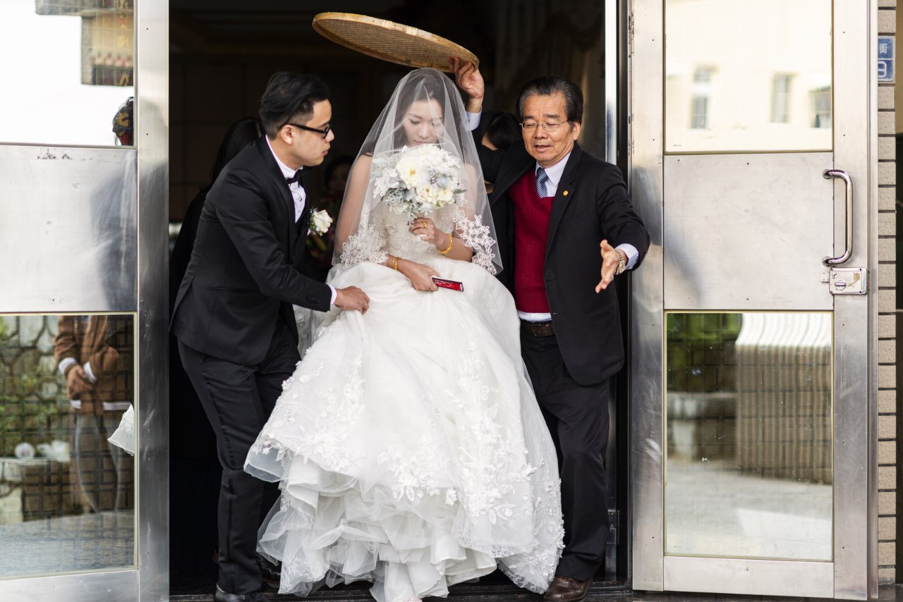 新娘在媒人與新郎陪同下出門,手捧捧花準備迎接婚禮