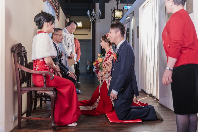 新郎穿著西裝，新娘穿著龍鳳褂跪在父母面前進行傳統拜別儀式，現場氛圍莊重
