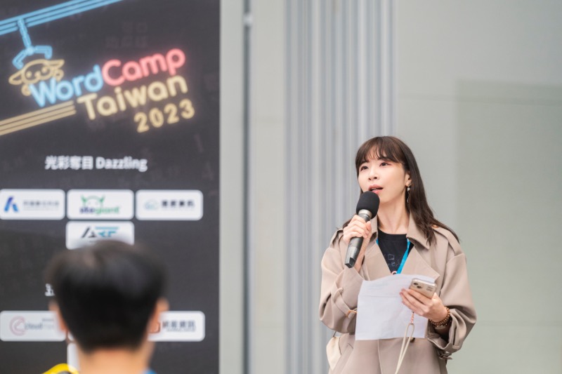 WordCamp Taiwan 2023 現場主持人手持麥克風發言，背景為會議活動看板。