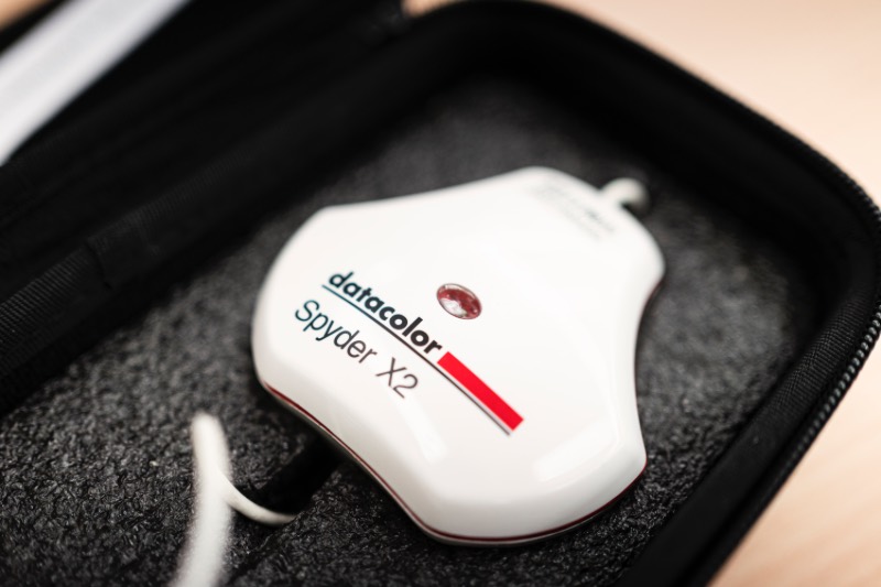 Datacolor Spyder X2 螢幕校色器本體放在黑色收納盒中，白色機身上有品牌標誌與紅色感光元件