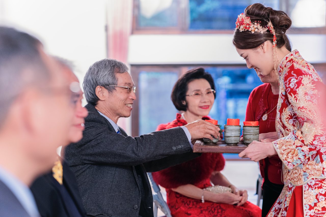 紅色中式禮服新娘在宜蘭掌上明珠餐廳奉茶給長輩，長輩微笑將紅包放入茶杯內，後方親友見證儀式。