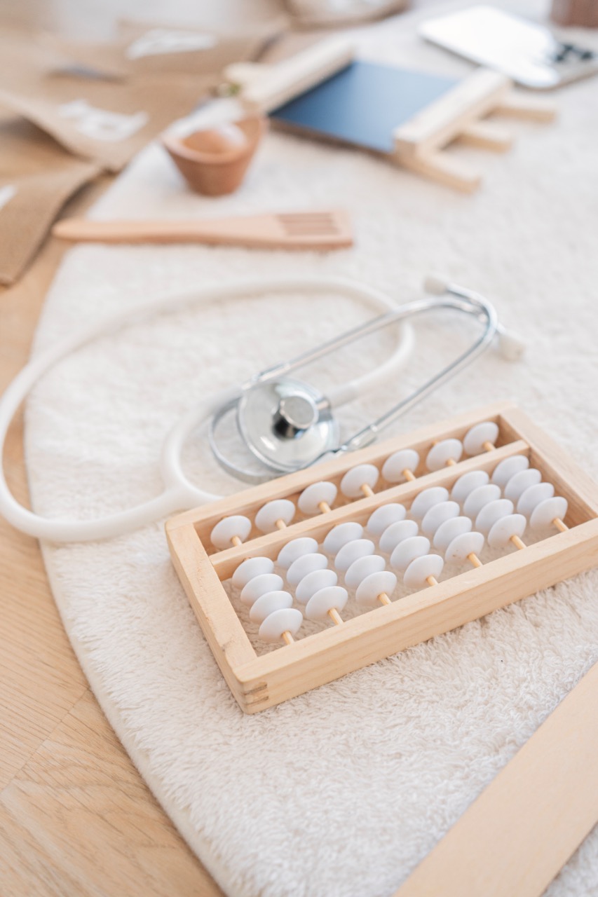 毛巾墊上放著聽診器與木製小算盤，周圍散落木製餐具與小道具，呈現抓周道具的近拍細節。